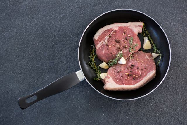 Sirloin chop and herbs in frying pan against black background