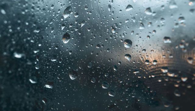 Moody Raindrops Clinging to Window Glass with Warm Bokeh Reflections