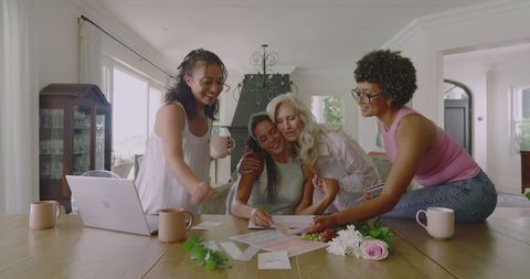 Women collaborating joyfully on wedding plans at cozy home