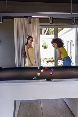 Diverse friends playing pool in modern game room wearing yellow sundress and lime top