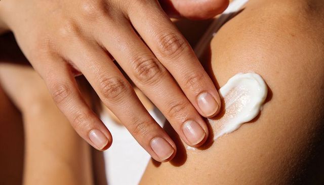 Applying moisturizer on upper arm by female hand, close-up skincare, healthy nails radiant glow