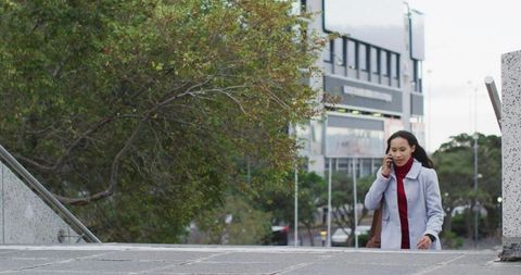 Young woman walking up city steps talking on phone wearing gray coat and red sweater
