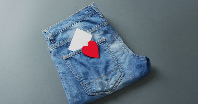 Close up of folded jeans with heart and white note on grey background with copy space. Denim day, material, style and design concept.