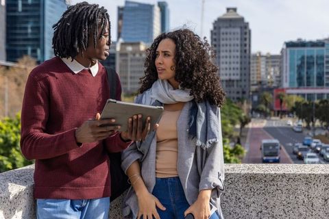 Multicultural friends discussing tablet on city terrace overlooking skyline and traffic