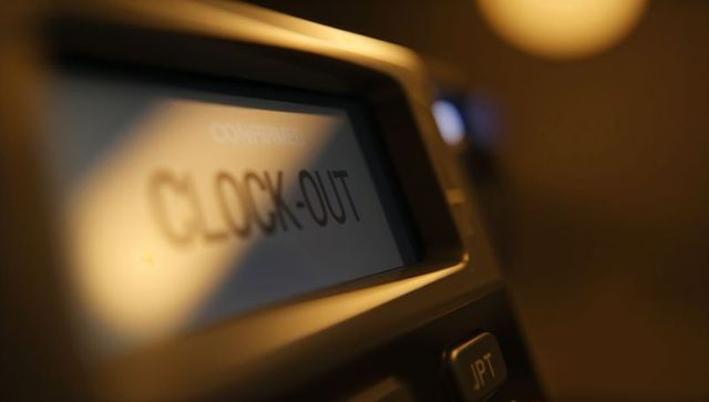 Backlit time clock display showing clock out on employee punch terminal with warm bokeh