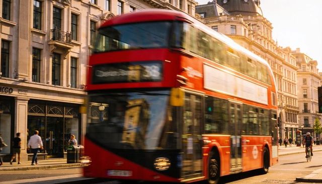 Red double-decker bus racing through sunlit london avenue with cyclist and pedestrians