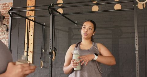 Female workout partners hydrating and chatting during strength training in industrial gym