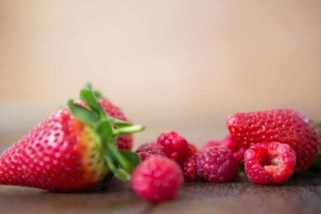This image showcases a close-up view of fresh strawberries and raspberries on a wooden board. The vibrant red colors and natural textures make it ideal for use in food blogs, healthy eating promotions, recipe books, and advertisements for organic produce. It can also be used in summer-themed designs and nutritional guides.