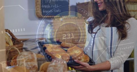 Smiling baker holding tray of sesame rolls and loaves in bakery with chalkboard display