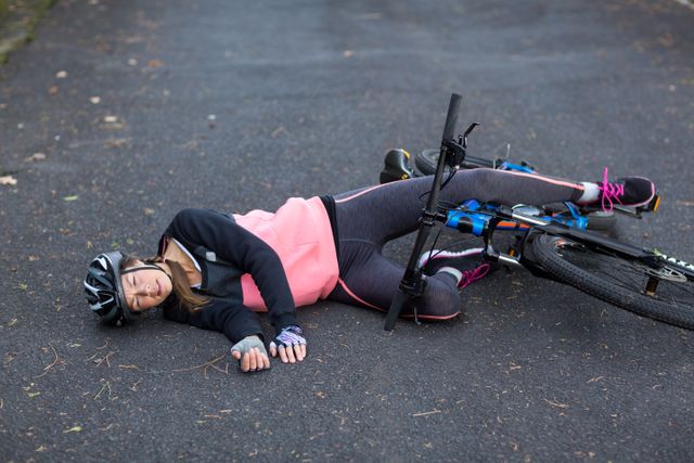 Female biker fallen from her mountain bike on the road