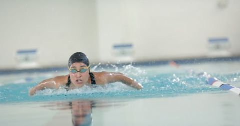 The image captures an athlete swimming freestyle in a pool, creating visible splashes in the water. This active and dynamic photo is ideal for use in articles and promotional materials related to swimming competitions, swim training, or athletic events. It can also be used by fitness magazines or swim clubs to illustrate powerful swimming techniques and sportsmanship.