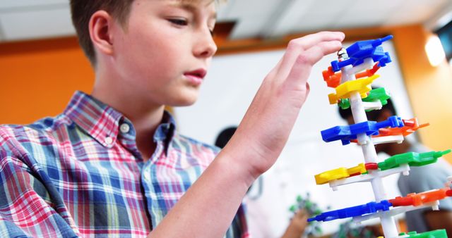 Young boy working on DNA model with colorful pieces. Ideal for education content, classroom resources, and STEM-related themes. Good for promoting interactive learning and science activities for children.