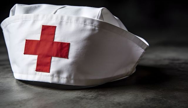 White nurse cap with red cross closeup on dark tabletop evoking nursing tradition