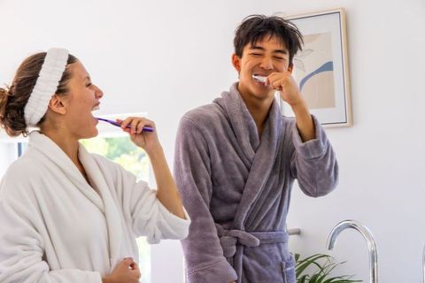 Diverse young couple brushing teeth together in robes during morning bathroom routine
