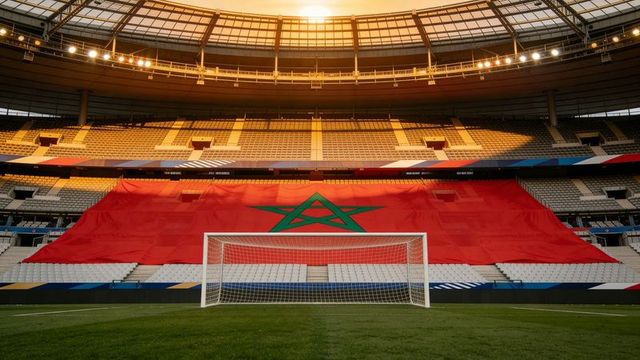 Giant moroccan flag draping stadium stands behind goal on sunlit football pitch