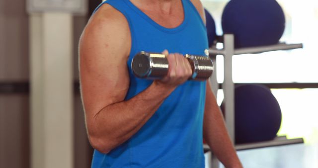 A middle-aged Caucasian man is working out with a dumbbell, focusing on his bicep curl exercise. His commitment to fitness is evident in his muscular build and concentrated effort.