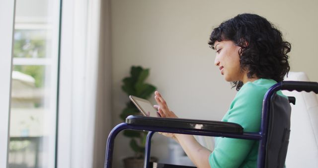 Thoughtful biracial disabled woman in wheelchair using tablet in living room - Download Free Stock Photos Pikwizard.com