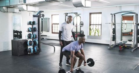 Trainer guiding client in lifting barbell for strength training