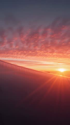 Shooting vertical sunrise from airplane window capturing glowing wing and cloudscape