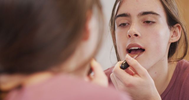 A young woman applies lip gloss while looking in the mirror. Perfect for blogs, articles, or advertisements about beauty, makeup tutorials, self-care routines, or promoting cosmetic products.
