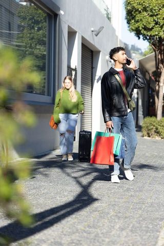Urban shoppers walking with luggage and colorful shopping bags while calling on smartphone