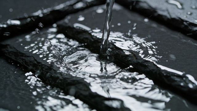 Pouring water forming concentric ripples on dark grooved slate surface