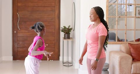 African mother and daughter dancing together in home entryway wearing pink activewear