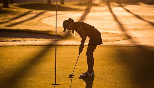 Female golfer lining up putt at golden hour backlit silhouette on green