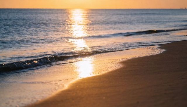 Golden sunrise reflections on wet sand with gentle waves along calm ocean shoreline