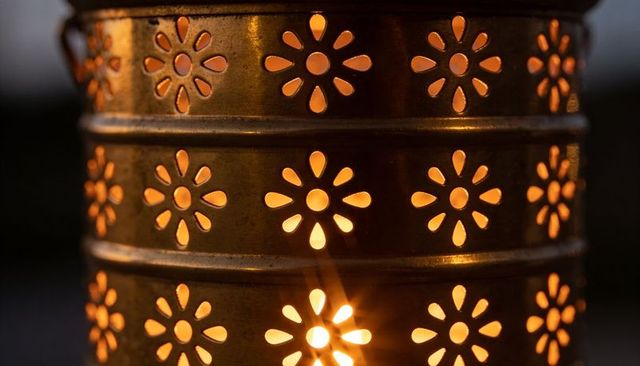 Bronze lantern casting warm floral glow through daisy cutouts with aged patina
