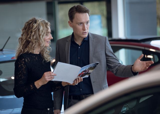 Female customer showing brochure to salesman in car showroom 