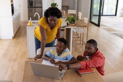 African american family helping son with homework using laptop at kitchen table