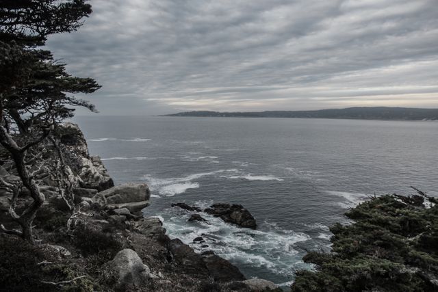 Dramatic coastal landscape featuring rocky cliffs overlooking waves crashing against the shore. Overcast sky creates a somber and moody atmosphere. Ideal for projects involving travel, nature, and outdoor activities, as well as conveying themes of solitude, wilderness, and natural beauty.
