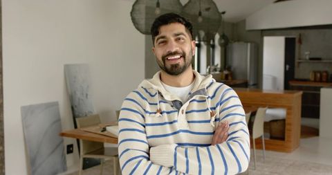 Confident indian man standing with arms crossed smiling in modern kitchen interior