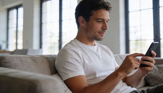 Man using smartphone on sofa in bright minimalist loft with grid windows