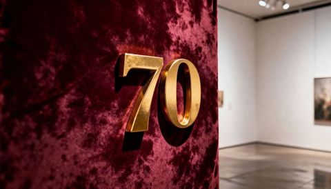 Gleaming gold number 70 catching warm light on burgundy velvet panel in art gallery