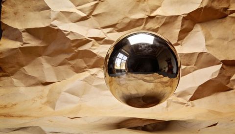 Hovering chrome sphere reflecting window grid over crumpled kraft paper backdrop warm glow