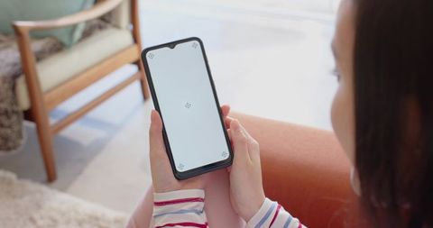Asian woman holding smartphone with blank screen on rust sofa in cozy living room