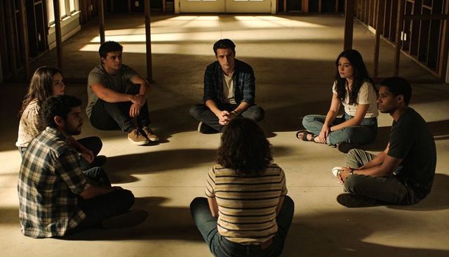 Young adults sitting in circle on concrete floor of unfinished building in warm sunlight