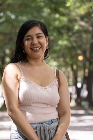 Smiling woman standing on sunlit park walkway wearing camisole and gold hoops
