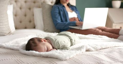 Mother Working Remotely with Sleeping Baby on Bed