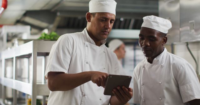 Two diverse male chefs talking and using tablet in restaurant kitchen. Working in a busy restaurant kitchen.