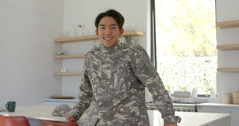 Smiling asian soldier in modern kitchen with mug
