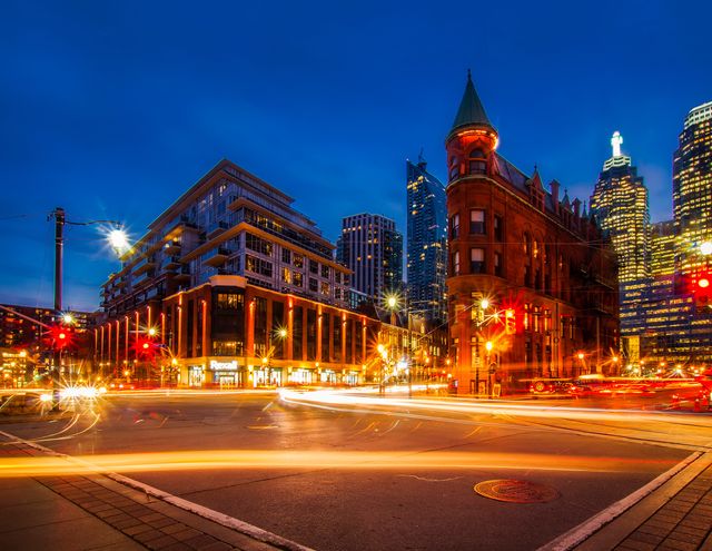 Downtown Toronto with bustling traffic lights streaking through the intersection at dusk. The modern and historic architecture creates a dynamic skyline. This image is excellent for projects related to urban living, travel, city infrastructure, and night photography.