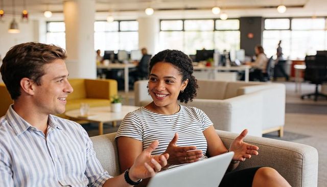 Coworkers collaborating on laptop while discussing ideas on modern office lounge sofa