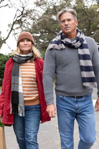 Mature couple walking together on overcast sidewalk wearing cozy scarves and casual jeans