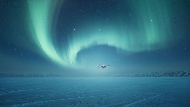 Drone hovering over frozen arctic plain under vibrant northern lights display