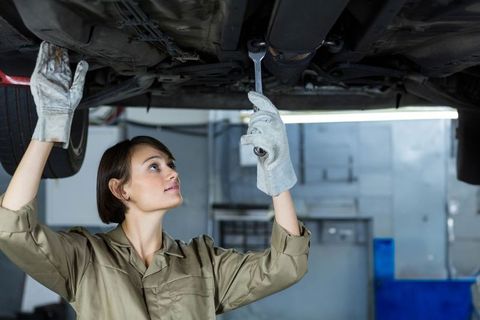 Female mechanic inspecting vehicle chassis using wrench in modern garage