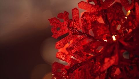 Sparkling red snowflake ornament closeup with warm bokeh holiday light decorative bauble