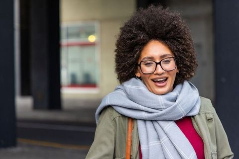 Laughing african american woman wearing light-gray scarf and glasses on urban street
